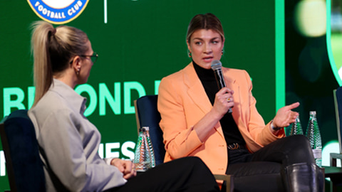 Flo Edwards seated on a stage with a microphones, talking