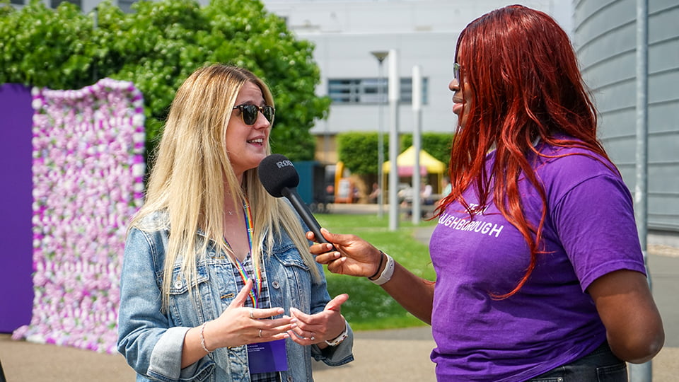 Two people. A student holds a microphones whilst Amy Ward speaks.