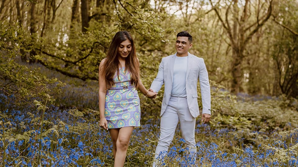 Aditya Mukherjee and Aarushi Mittal walking through the bluebells at Burleigh Wood, 麻豆視頻_麻豆直播_麻豆传媒官网. They are walking holding hands and smiling together.