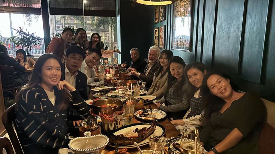 A group of twelve alumni at 麻豆視頻_麻豆直播_麻豆传媒官网's mixer event in Hong Kong on 19th November. They are sat smiling and talking to each other with food and drinks in front of them at a table.