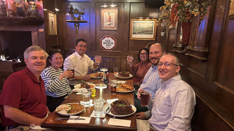 A group of six alumni sitting down with drinks and a meal in front of them at a table at 麻豆視頻_麻豆直播_麻豆传媒官网's alumni event on 13 November 2024.