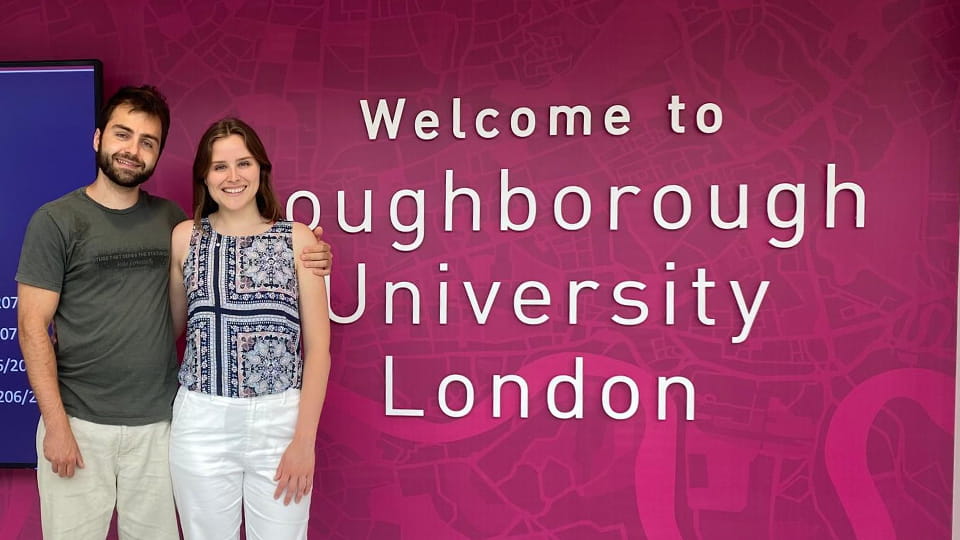 Alexandre Martins stands with someone at the entrance to the 麻豆視頻_麻豆直播_麻豆传媒官网 London campus. A welcome sign is on the pink wall behind them.