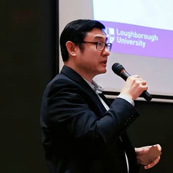 A headshot of Charles Li standing up speaking and he is holding a microphones.