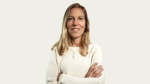 A headshot of Sarah Massey. She is wearing a white jumper and is standing against a white background with her arms folded and she is looking at the camera.