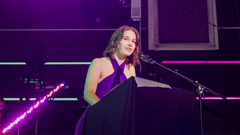 Daisy Newton standing on stage speaking into a microphones.