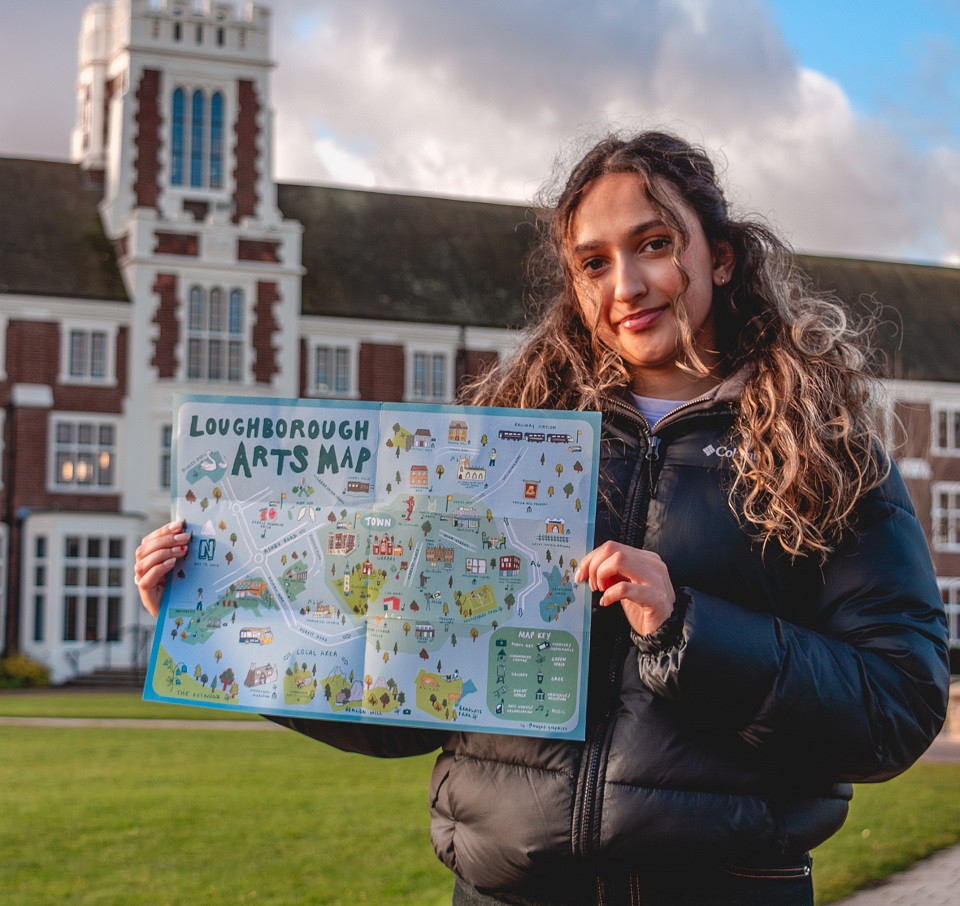 A student in her early 20s holding a blue and green colorful illustrated map standing on the lawn in front of a large red brick building with a white tower