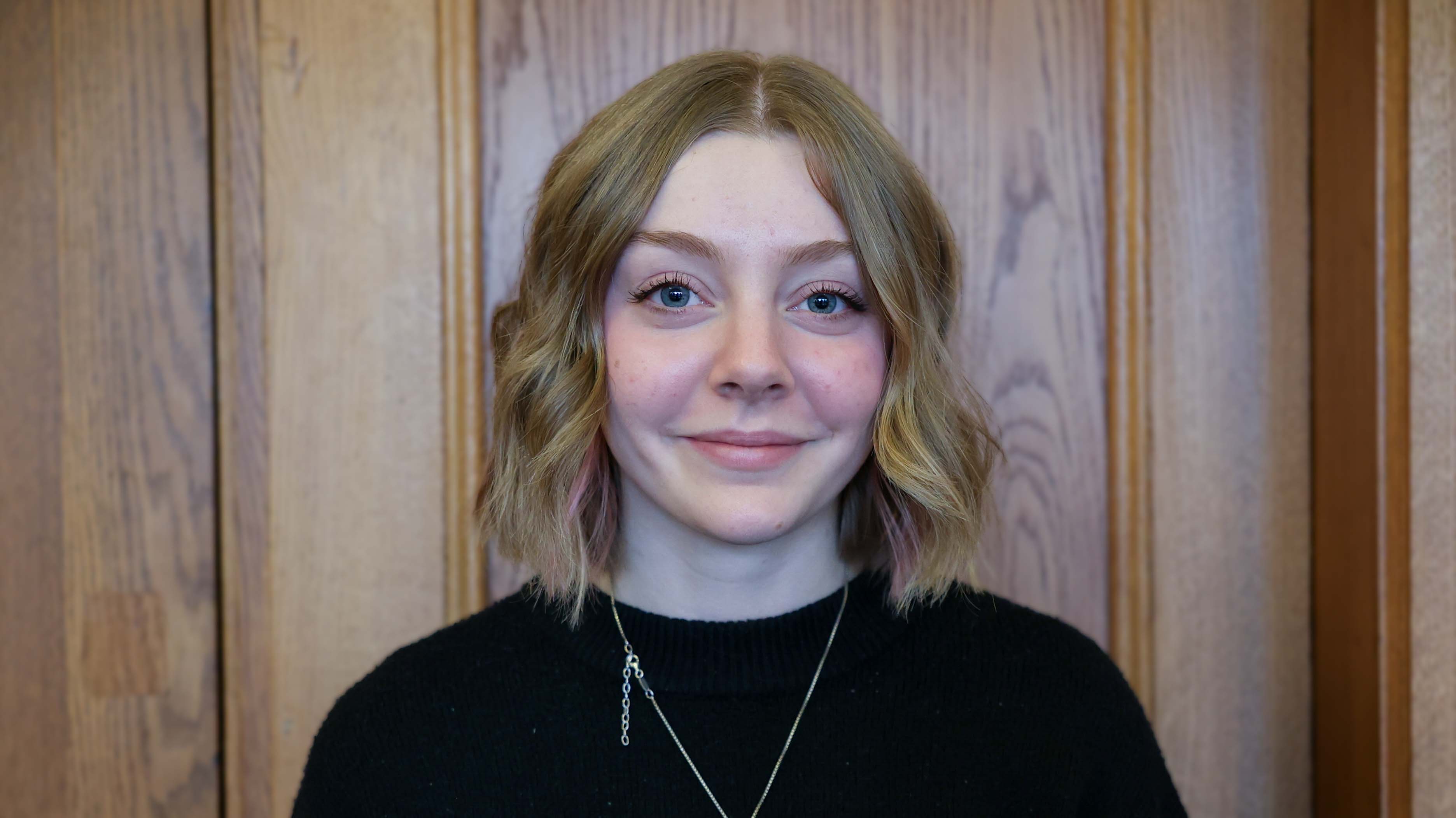 Young white female with short wavy dark blonde fair wearing black and a gold necklace