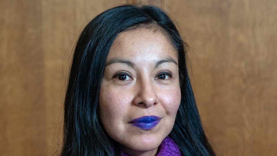 Female mature student of Latin American heritage with long black hair and purple lipstick