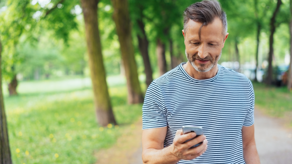 A middle aged man looks at his phones while taking a walk