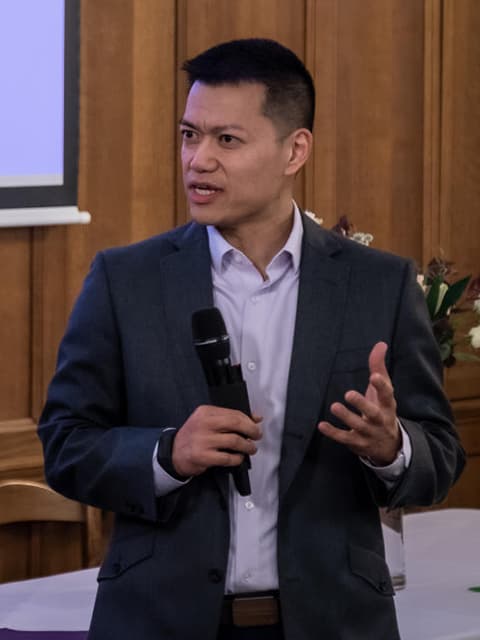Brian Yip giving a speech. He is wearing a suit and holding a microphones.
