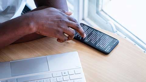 Someone scrolling on a smartphones screen with a laptop keyboard to the side.