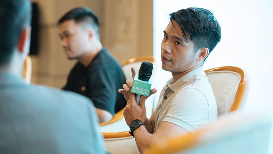 Leo Nguyen sitting at the conference table holding a microphones with the logo of Green Horizon.