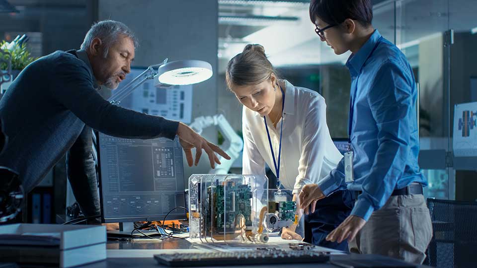 An image showing three people, two men and one woman, looking at a piece of technology