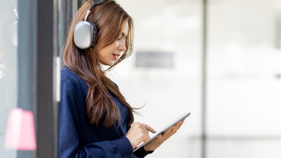 Female student with long red hair wearing headphoness and using a tablet computer