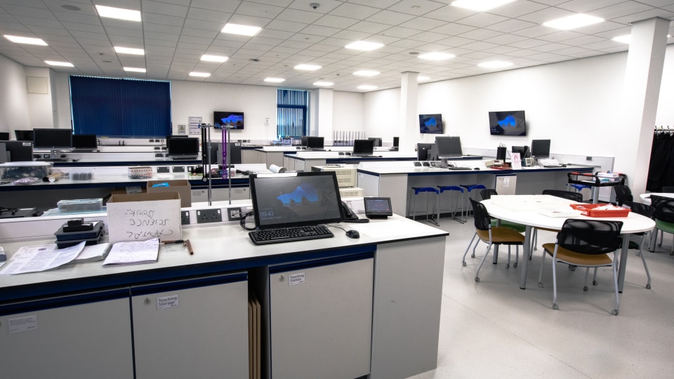 West Park Labs WPL104 - Spacious specalist lab with multiple workstations, monitors, and round tables. Bright lighting and blue blinds enhance the modern design.