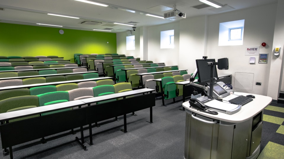 West Park Teaching Hub WPT004 - Lecture theatre with tiered seating in green and gray, a podium with computer and phones, and a bright green wall.
