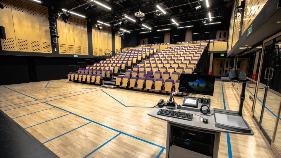 Martin Hall MHL001 - Large lecture theatre with tiered seating, wooden floor, and a teaching podium equipped with a computer and microphones.