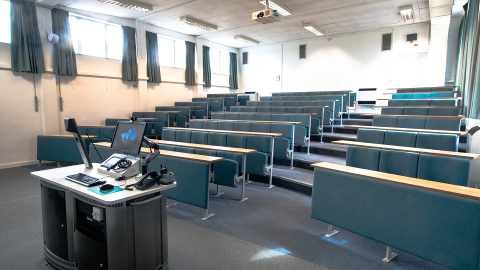 Schofield SCH001 - Lecture theatre with tiered seating, projector, and a lectern equipped with a computer and phones.