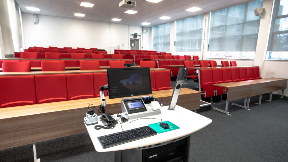 Schofield SCH101 - Lecture theatre with red tiered seating, large windows, and a lectern equipped with a computer and microphones.