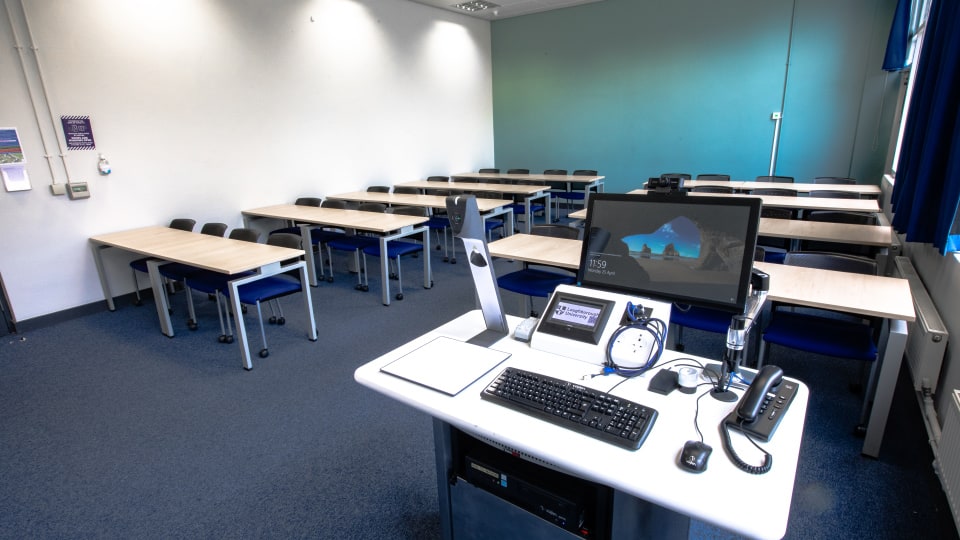 Wavy Top WAV040 - Teaching room with rows of tables and chairs, equipped with a computer station, keyboard, phones, and projector control panel.