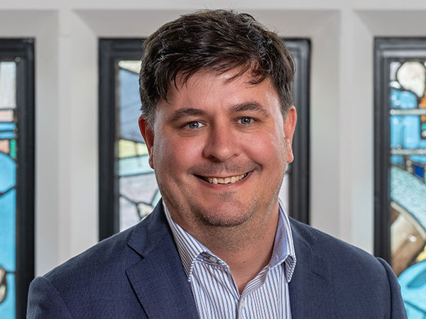 A portrait photograph of Professor Dan Parsons against a stained glass background