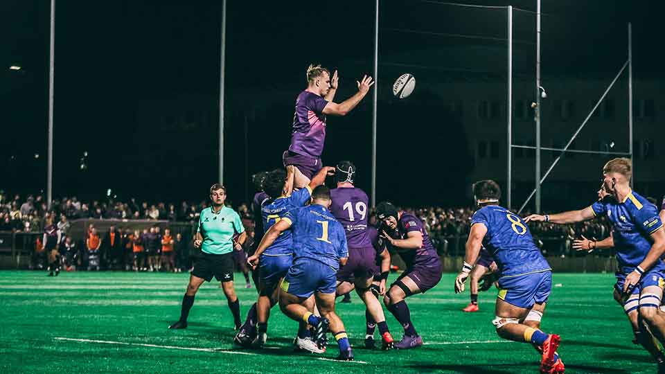 Rugby players playing on a pitch under the lights after dark