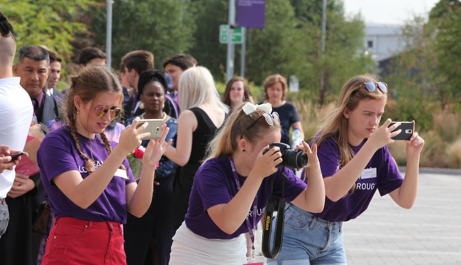 Three student ambassadors, wearing purple T-shirts, taking photos with their mobiles phoness and a camera.