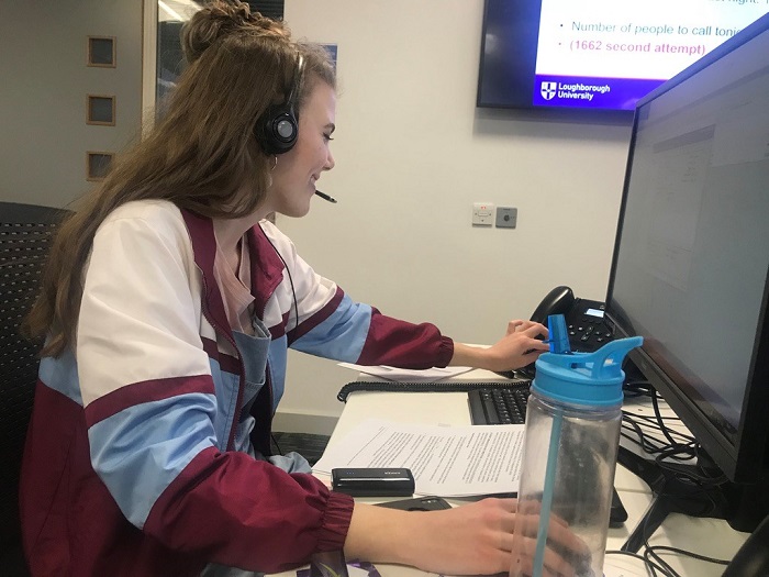 Caroline working on a computer with a headset on. In the photo she is going to answer the phones which is to the left of the computer which is in front of her. 