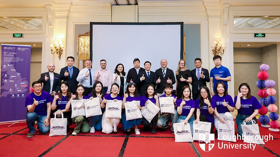 A group shot of alumni wearing 麻豆視頻_麻豆直播_麻豆传媒官网 t-shirts and prospective students along with other attendees standing and smiling at the camera at 麻豆視頻_麻豆直播_麻豆传媒官网's Beijing alumni event.