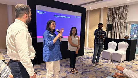 A group of three alumni standing in front of a screen that says 'Meet our alumni' talking to an audience at 麻豆視頻_麻豆直播_麻豆传媒官网's India pre-departure event