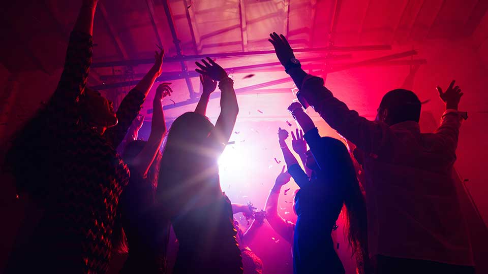 A group of friends partying in a nightclub. The lights are pink and purple.