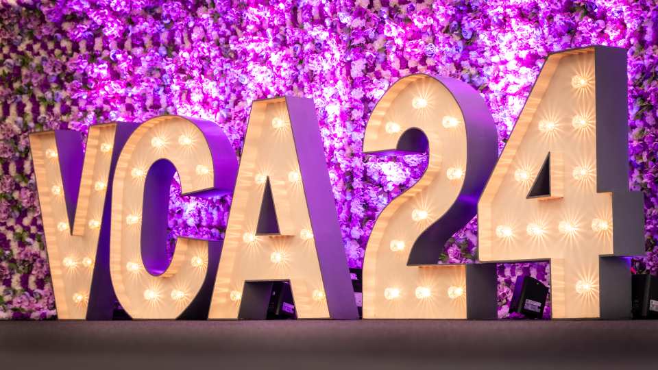 Large light up letters 'VCA24' with a backdrop of purple flowers behind.